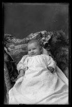 Portrait of infant in dress in bassinet with embroidered cushion