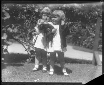 Two girls standing, holding puppies in grassy yard