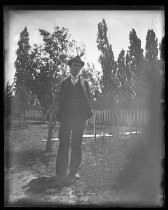 Man in three piece suit, and hat, standing in back yard