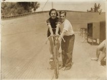 Woman on bicycle, man assisting