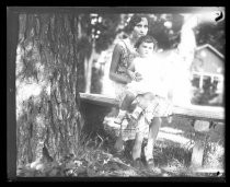 Woman and toddler seated on bench under tree