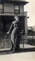 Unidentified woman outside of house with wrought iron fence