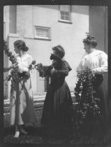 Three women posing with flower garlands and a black cat