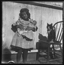 Girl with doll, cat sitting on a chair