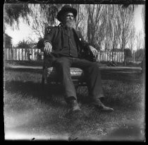 Man seated outdoors, wearing three-piece suit and hat