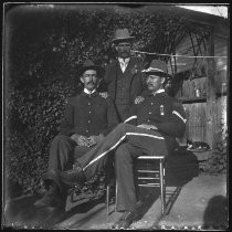 Three men posing outdoors, one in military uniform