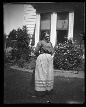 "Mrs. H.K.R." standing in yard, wearing a gingham apron