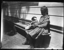 Young girl in calico dress, sitting on bench, holding a dog