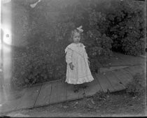 Young child in dress, standing on wooden walkway, c. 1912