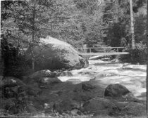 Foot bridge over rocky river in forest, c. 1912