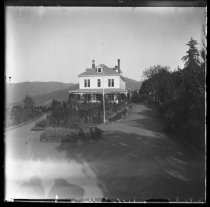 Large, two-story house set on a hill, with curved driveway