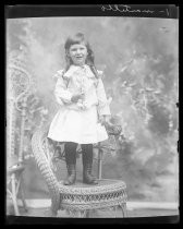 Portrait of a child in white dress standing on wicker chair
