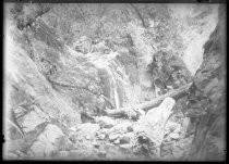 Two men seated in front of rocks with waterfall