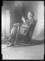 Man seated by fire in rocking chair, smoking pipe