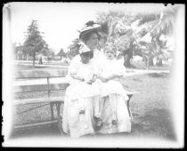 Woman holding two children on park bench, c. 1905