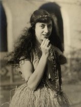 Young woman wearing grass skirt, holding prune