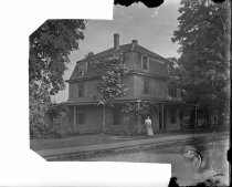 Woman in front of three-story house, seen from road, c. 1912