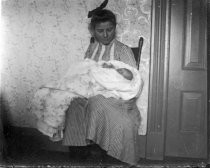 Woman, seated, holding baby in blankets, c. 1912