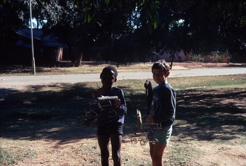 Portrait of Daniel Cancel and his friend Crispin, holding locally-made wire cars, in front of our university housing home in Lusaka