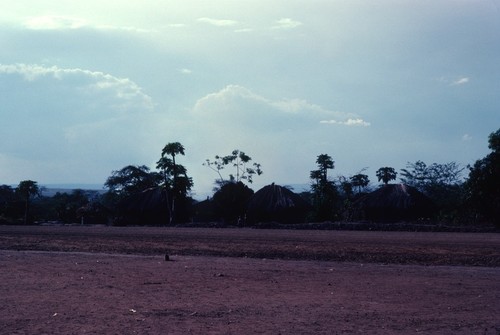 Main road into Kaputa village, from the east, with houses on the other side of the road and the hills of the Democratic Republic of the Congo in the background