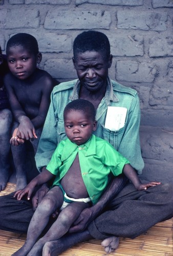 Mr. William Miusonda on veranda of his home, with children, at Kaputa village