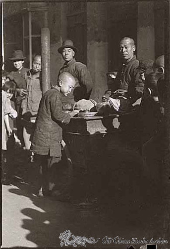 Children buying food from a street vendor on a street in Tientsin, winter 1946