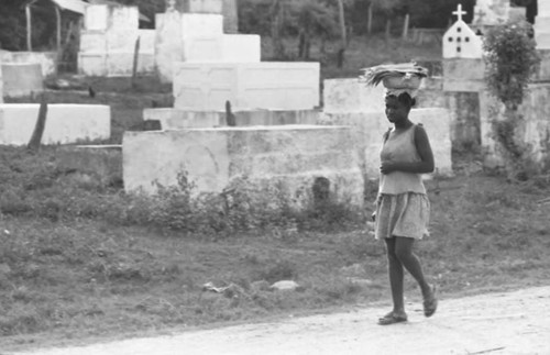 Woman with a bowl full of fish walks along a cemetery, San Basilio de Palenque, 1975
