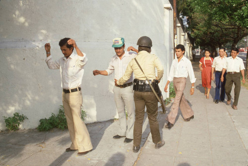 Soldier frisking people in the street, San Salvador, El Salvador, 1982