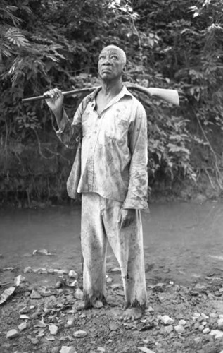 Fermín Herrera stands by the river with a rifle, San Basilio de Palenque, 1975