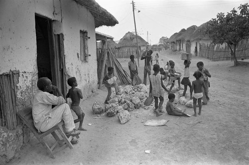 Small children pick up large boulders next to a building, San Basilio de Palenque, 1977