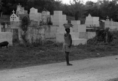 Woman with a bowl full of fish walks along a cemetery, San Basilio de Palenque, 1975