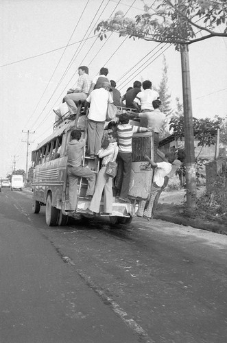 Civilians travelling through town on and in a city bus, San Salvador, circa 1980