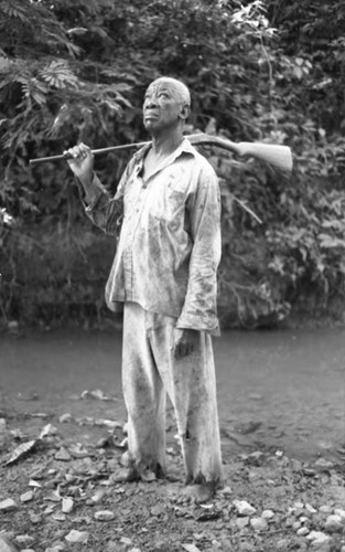 Fermín Herrera stands by the river with a rifle, San Basilio de Palenque, 1975