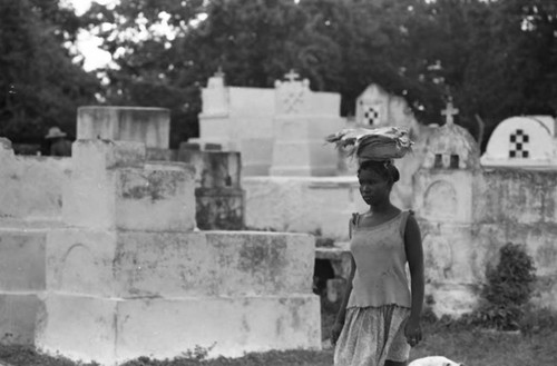 Woman with a bowl full of fish walks along a cemetery, San Basilio de Palenque, 1975