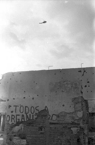 Army helicopter on patrol over a destroyed building, Perquín, 1983