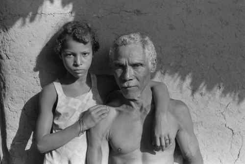 Man and girl standing in front of a house, San Basilio de Palenque, 1976