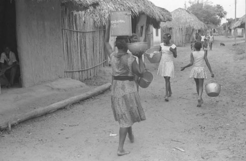 Women and children walk in the street in front of houses, San Basilio de Palenque, 1975