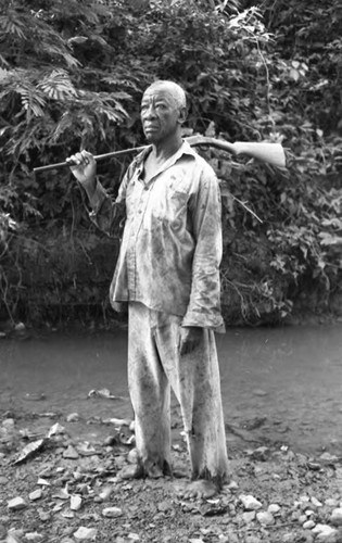 Fermín Herrera stands by the river with a rifle, San Basilio de Palenque, 1975