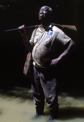 Fermín Herrera with rifle on his shoulder and feet in the water, San Basilio de Palenque, 1976