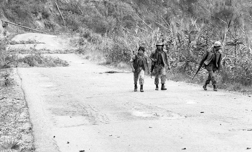 Three soldiers walking on a paved road, Guatemala, 1982