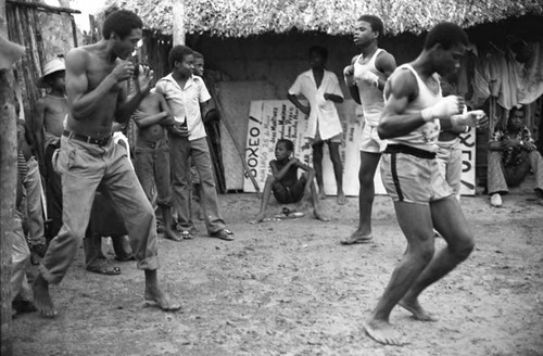 Three men boxing outdoor in front of a crowd, San Basilio de Palenque, 1975