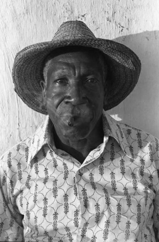 A man smokes and sits in front of a wall, San Basilio de Palenque, 1975