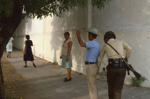 Soldier frisking people in the street, San Salvador, El Salvador, 1982