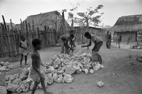 Small children pick up large boulders next to a building, San Basilio de Palenque, 1977