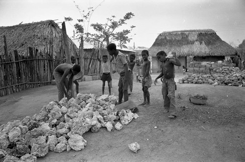 Small children pick up large boulders next to a building, San Basilio de Palenque, 1977