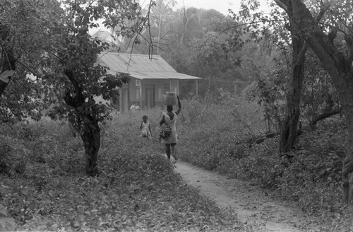 Woman walking with metal container on her head, San Basilio de Palenque, 1976