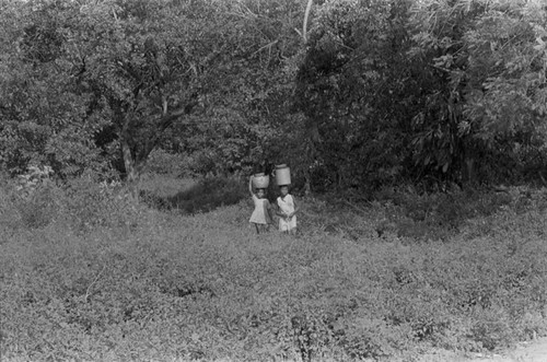 Two girls walking with a bucket on their head, San Basilio de Palenque, 1976