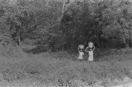 Two girls walking with a bucket on their head, San Basilio de Palenque, 1976