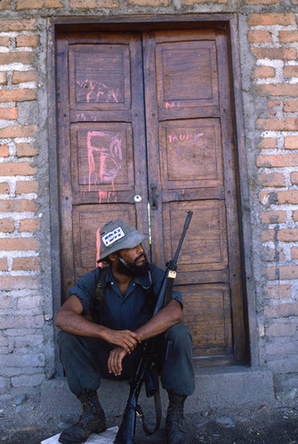 A Contra soldier sits in front of a house, Nicaragua, 1983