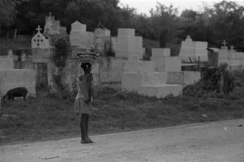 Woman with a bowl full of fish walks along a cemetery, San Basilio de Palenque, 1975